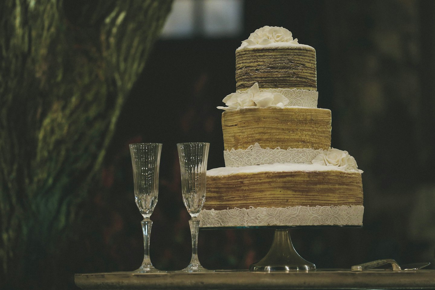 Elegantná trojpodlažná svadobná torta s bielou čipkou na striebornom stojane.
